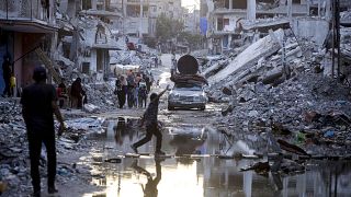 FILE - Palestinians displaced by the Israeli air and ground offensive on the Gaza Strip, walk past sewage flowing into the streets of the southern town of Khan Younis.