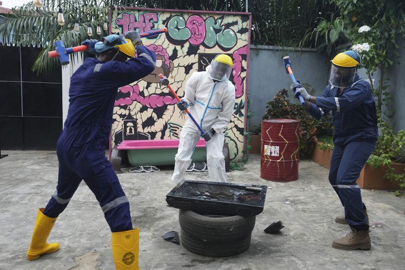 People wearing protective gear use sledgehammers to break a television set to vent their anger outside the Shadow Rage Room in Lagos, Nigeria, Sunday, July 28, 2024. 