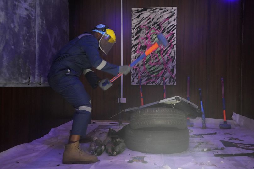 Olaribigbe Akeem, wearing protective gear, uses a sledgehammer to break a television set to vent his anger inside the Shadow Rage Room in Lagos, Nigeria, Sunday, July 28, 2024