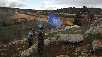 Elementos da ONU seguram a sua bandeira, enquanto observam as escavadoras israelitas a tentar destruir túneis construídos pelo Hezbollah, perto da aldeia de Mays al