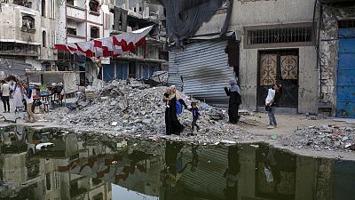 Palestinianos deslocados pela ofensiva aérea e terrestre israelita na Faixa de Gaza caminham ao lado de uma linha escura de esgotos que corre nas ruas da cidade de Khan Younis, no sul do país