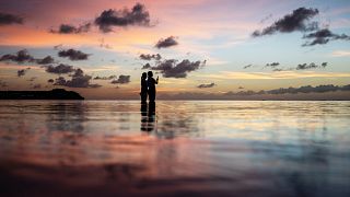 Tourists watch the sun set along a popular beach in Tamuning, Guam.