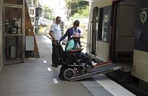 A volunteer for the Paris 2024 Olympic and Paralympic Games navigates a ramp to join a RER train with the help of rail agents