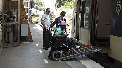 A volunteer for the Paris 2024 Olympic and Paralympic Games navigates a ramp to join a RER train with the help of rail agents