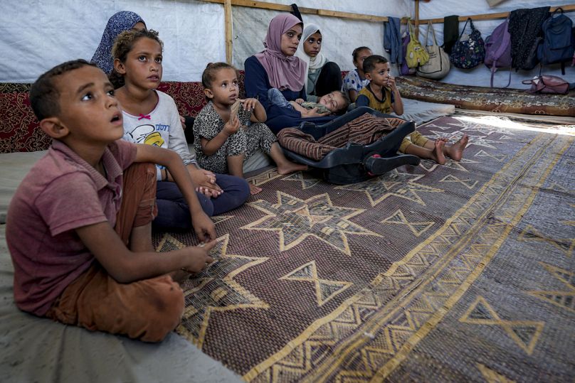 Displaced infant Abdel-Rahman Abu El-Jedian, 11-month-old, who suffers from polio, is carried by his mother, center, at a makeshift tent camp in Deir al-Balah, central Gaza St