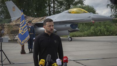 O Presidente da Ucrânia, Volodymyr Zelenskyy, responde a perguntas da imprensa em frente a um caça F-16 num local não revelado na Ucrânia, 4 de agosto de 2024