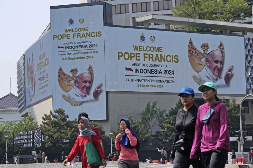 People walk past a welcoming signboard for Pope Francis displayed at Jakarta Cathedral in Jakarta, Indonesia, Sunday, Sept. 1, 2024, ahead of his visit to Indonesia from Sept.