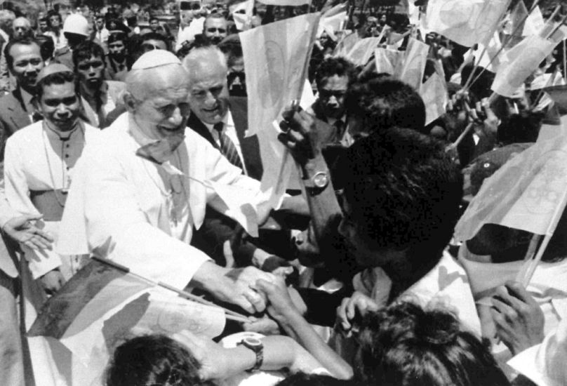 Esta fotografia de arquivo de 12 de outubro de 1989 mostra o Papa João Paulo II a apertar a mão a estudantes locais que agitam uma bandeira à sua chegada a Díli, Timor-Leste. 