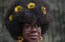 Uma mulher com girassóis no cabelo espera para entrar na passerelle de um desfile de moda de penteados afro em Havana, Cuba, sábado, 31 de agosto de 2024.