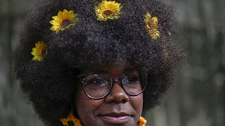 Uma mulher com girassóis no cabelo espera para entrar na passerelle de um desfile de moda de penteados afro em Havana, Cuba, sábado, 31 de agosto de 2024.