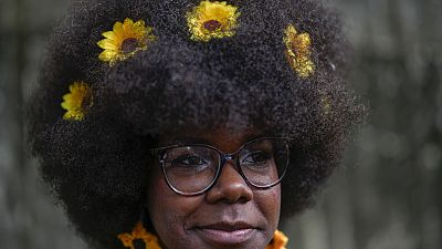 Uma mulher com girassóis no cabelo espera para entrar na passerelle de um desfile de moda de penteados afro em Havana, Cuba, sábado, 31 de agosto de 2024.