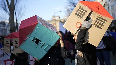 Δύο νεαρές γυναίκες φορούν χάρτινα σπίτια στα κεφάλια τους κατά τη διάρκεια διαδήλωσης διαμαρτυρίας για την κρίση στέγασης στην Πορτογαλία, στη Λισαβόνα, 27 Ιανουαρίου 2024.