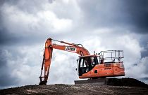 An orange construction excavator digging on an overcast day