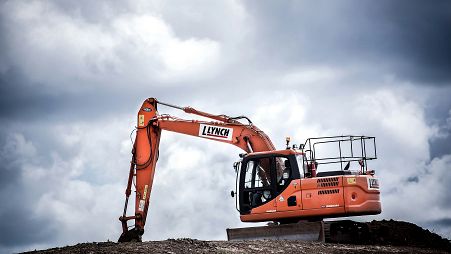 An orange construction excavator digging on an overcast day