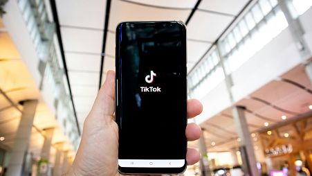 A person holding a smartphone displaying the TikTok application logo