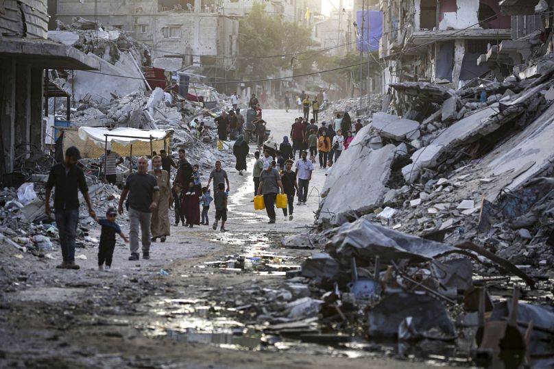 Palestinos desplazados caminan por una oscura franja de aguas residuales que fluyen hacia las calles de la ciudad sureña de Jan Yunis, julio de 2024.