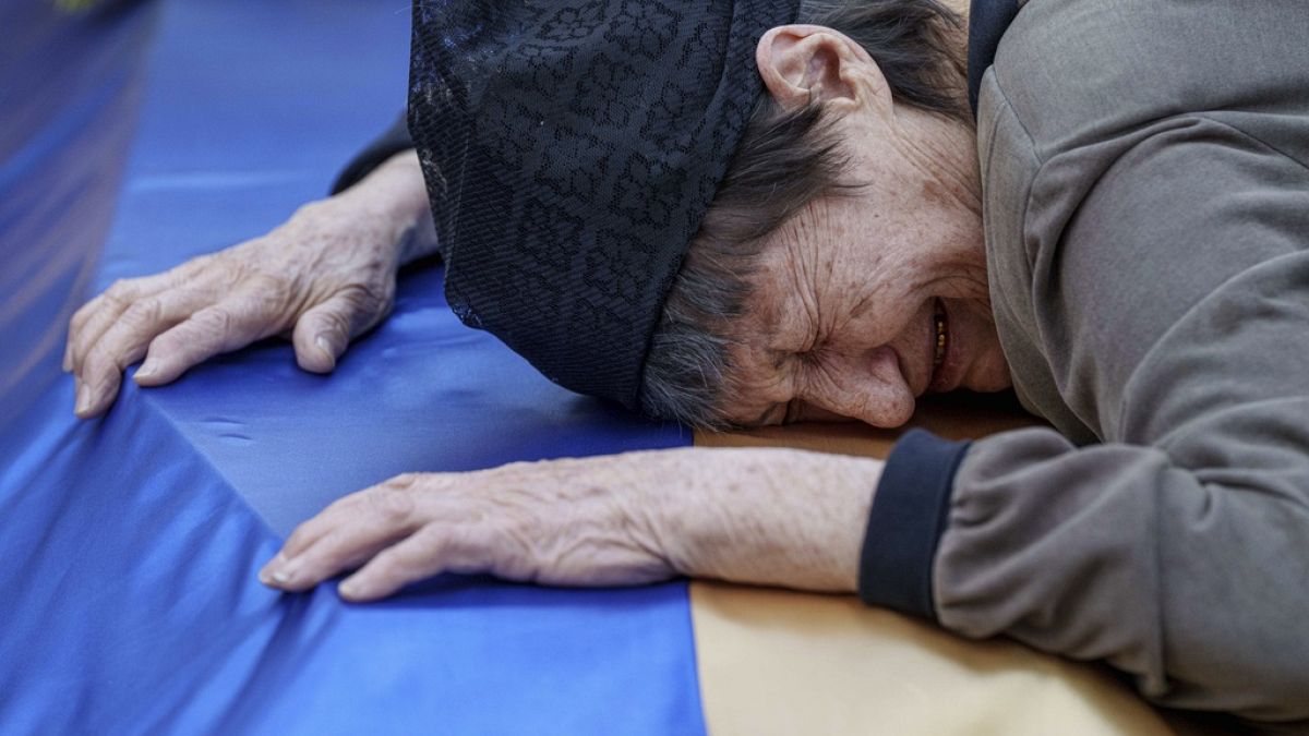 An old Ukrainian mourning on a coffin with Ukranian flag