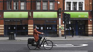 Bir kadın Londra'daki bir iş merkezinin önünden bisikletle geçiyor