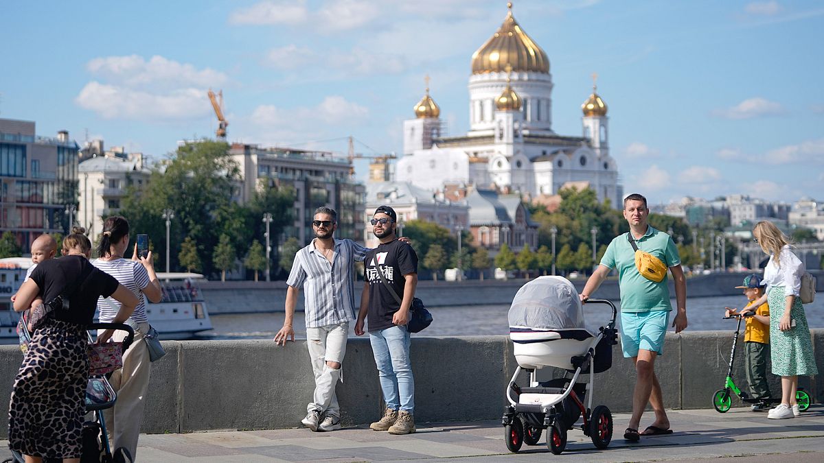 People walk on Krymskaya embankment of Moskva river with the Cathedral of Christ the Saviour in the background, in Moscow, 16 August 2024