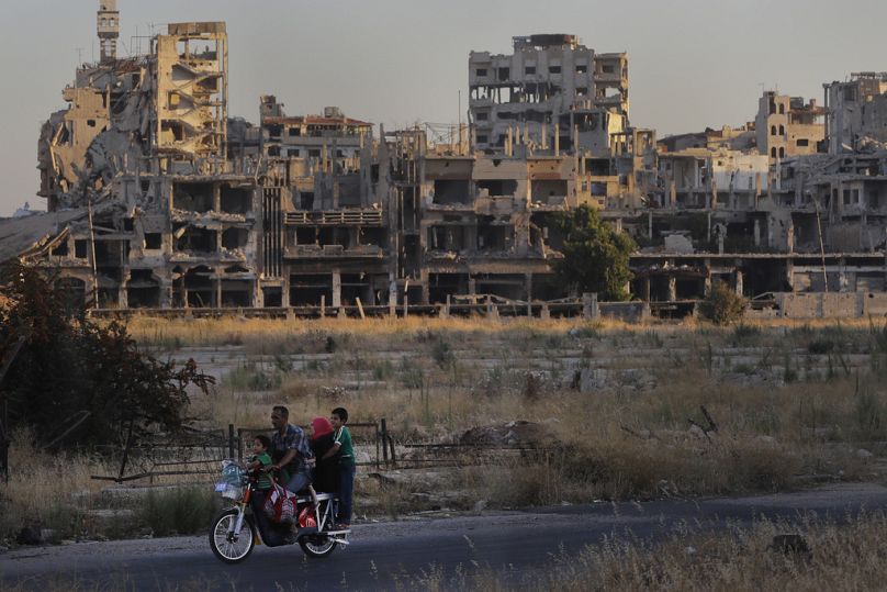 People ride their motorcycle by damaged buildings in the old town of Homs, August 2018