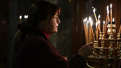 Une femme allume une bougie pendant la Divine Liturgie de Noël, dans l'église orthodoxe grecque de Panagia (Vierge Marie) Kapnikarea à Athènes, 25 décembre 2023.