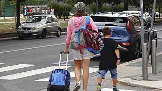 Uma mulher carrega mochilas enquanto o seu filho caminha depois de sair de uma escola primária, em Milão, Itália, quarta-feira, 14 de setembro de 2022.