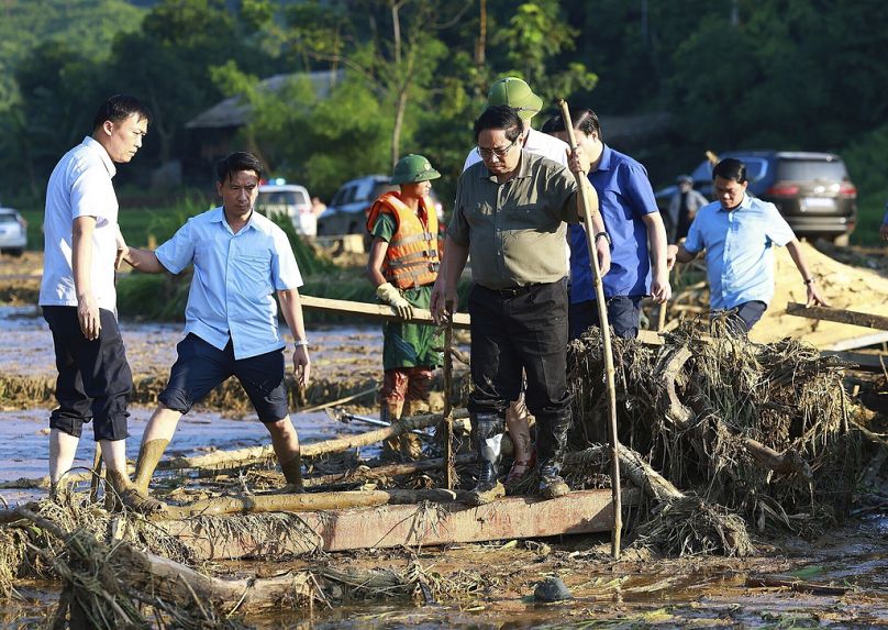 Vietnam's Prime Minister Pham Minh Chinh, foreground right, visits as rescue work is underway after a flash flood buries a hamlet in mud and debris