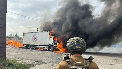 Un officier de police regarde un véhicule de la Croix-Rouge en feu qui a été détruit lors d'une attaque russe à Donetsk, le 12 septembre 2024.