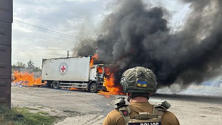 Um agente da polícia observa um veículo da Cruz Vermelha em chamas, destruído num ataque russo em Donetsk, em 12 de setembro de 2024