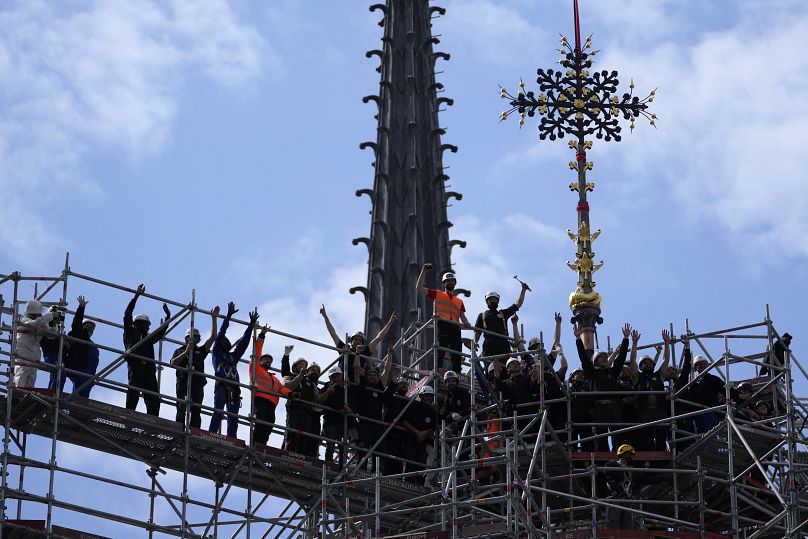 Des ouvriers célèbrent la réinstallation de la Croix du Chevet de la cathédrale Notre-Dame de Paris, à droite, le vendredi 24 mai 2024, à Paris.