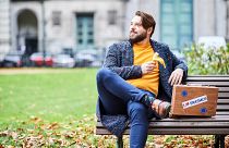 Young man on bench with a suitcase displaying the Erasmus logo (21/10/2019)