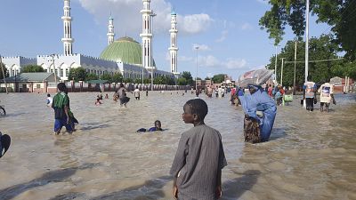 People walk through floodwaters following a dam collapse in Maiduguri, Nigeria, Tuesday Sept 10, 2024.