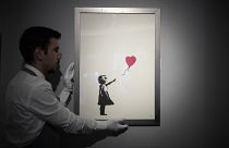 Un membre du personnel pose pour des photos avec une impression de "Girl with Balloon, 2004" de l'artiste de rue britannique Banksy à la maison de vente aux enchères Bonhams à Londres, le 8 novembre 2021.