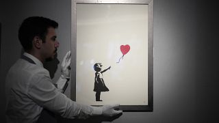 Bir personel, Londra'daki Bonhams müzayede evinde İngiliz sokak sanatçısı Banksy'nin 'Balonlu Kız, 2004' adlı eserinin baskısıyla poz veriyor, 8 Kasım 2021