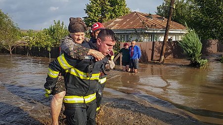 A rescuer carries a woman in Pechea, Romania, Saturday, Sept. 14, 2024 after torrential rainstorms left scores of people stranded in flooded areas