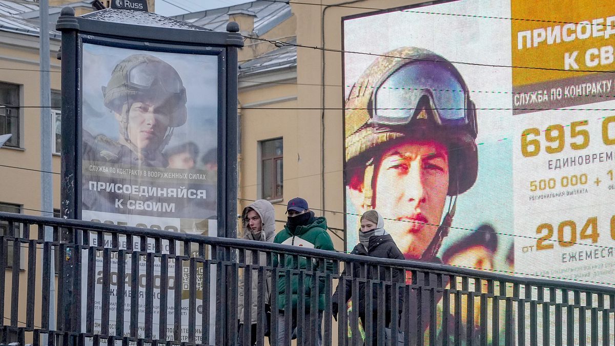 Des jeunes passent devant un panneau publicitaire et un écran qui promeuvent le service militaire contractuel dans l'armée russe, à Saint-Pétersbourg, le 22 novembre 2023.