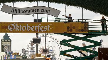 Arbeiter stehen auf einer Hebebühne während der Bauarbeiten auf dem Oktoberfestgelände am Haupteingang des Festes in München, Deutschland