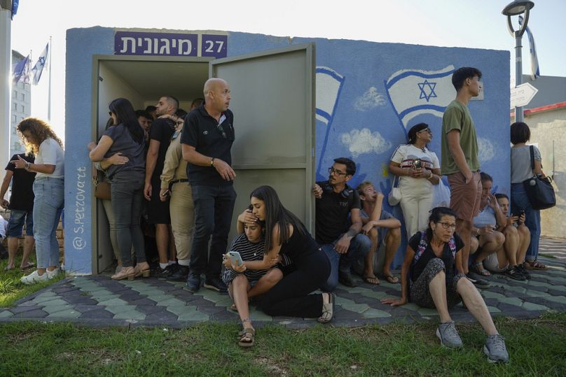 Israelis take cover next to a shelter as a siren sounds a warning of incoming rockets fired from Lebanon, in Nahariya, northern Israel, Thursday, Sept. 19, 2024. 