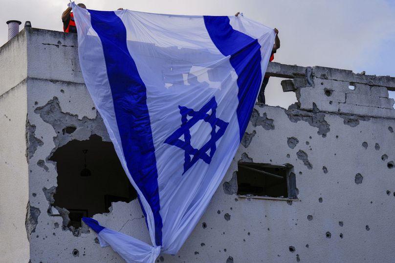 Municipality workers hang an Israeli flag over a damaged building that was hit by a rocket fired from Lebanon, in Kiryat Bialik, northern Israel, on Sunday, Sept. 22, 2024.