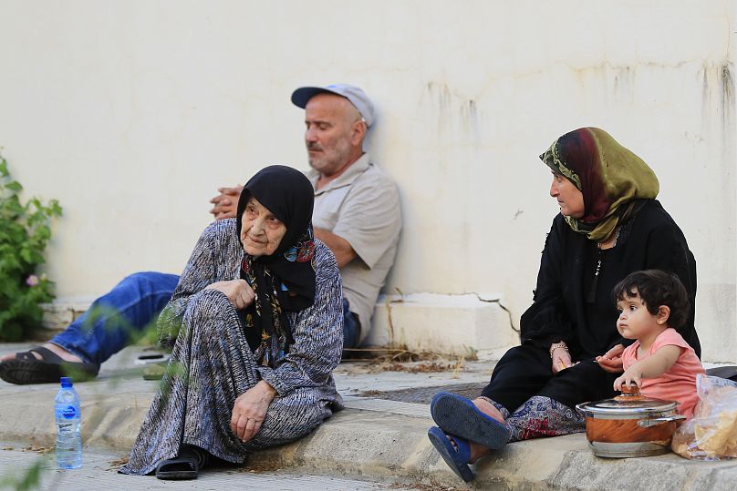 Pessoas que fogem das aldeias do sul do país, no meio dos ataques aéreos israelitas, sentam-se no passeio em frente a uma escola em Sidon. 