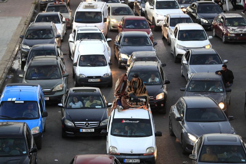 Lebanese citizens who fled the southern villages amid ongoing Israeli airstrikes Monday, sit on their cars at a highway that links to Beirut city, in the southern port city of