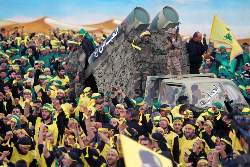 Hezbollah fighters stand atop a truck mounted with mock rockets as supporters chant slogans during a rally