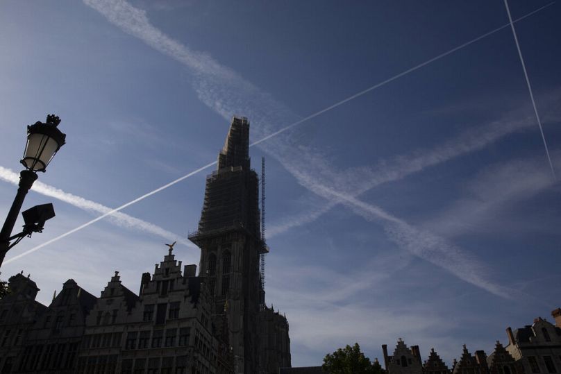 Buildings in the old town main square are silhouetted against a sky with airplane contrails in Antwerp, Belgium.