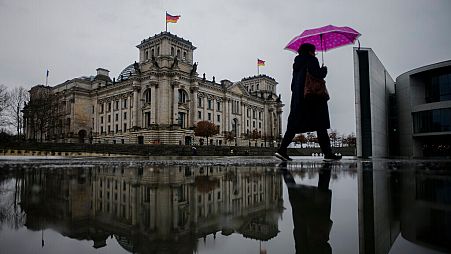 A person with an umbrella walks through the government district in front of the Reichstag building, the house of German parliament Bundestag,in Berlin, Germany, 2022.