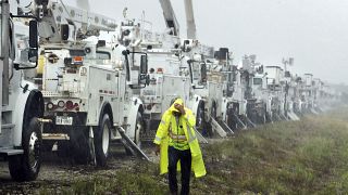 Bir vatandaş Helene Kasırgası'nın yol açacağı hasara hazırlık amacıyla bir tarlada bulunan elektrik hattı kamyonlarının yanından geçerken yağmur altında kalıyor, 26 Eylül 2024