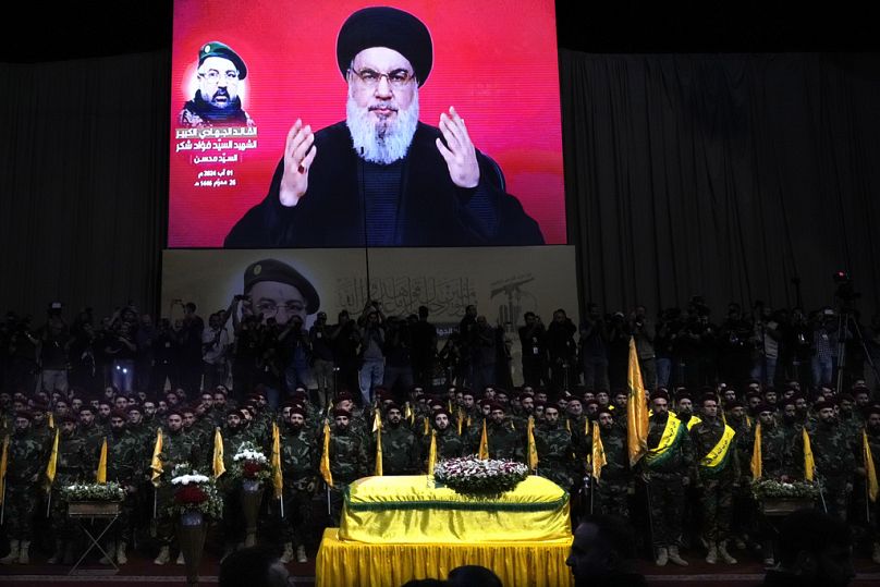 Des combattants du Hezbollah derrière le cercueil de leur commandant Fouad Shukur, tué par une frappe aérienne israélienne le 30 juillet, Nasrallah parle à travers un écran.