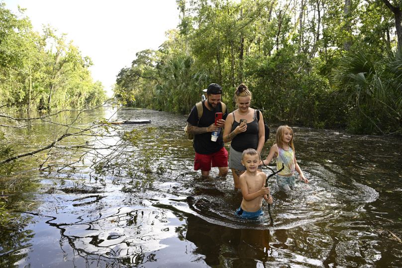 Dustin Holmes, a sua namorada Hailey Morgan e os seus filhos Aria Skye Hall, à direita, e Kyle Ross, caminham numa estrada inundada, Crystal River, Florida, 27/09/2024 