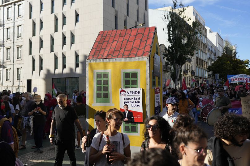 Ativistas empurram um edifício simulado com cartazes de estilo imobiliário com fotografias do primeiro-ministro Luís Montenegro durante um protesto em Lisboa, a 28/09/2024