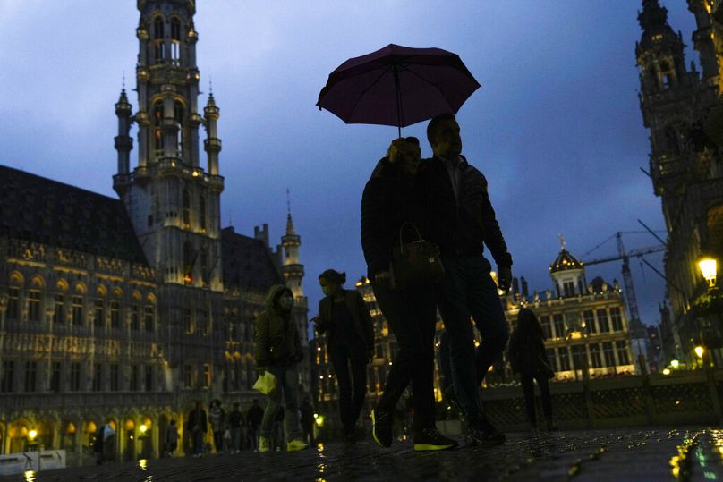 Pedestrians shelter with an umbrella against the rain at the Grand Place or Grand square in downtown Brussels, June 2021