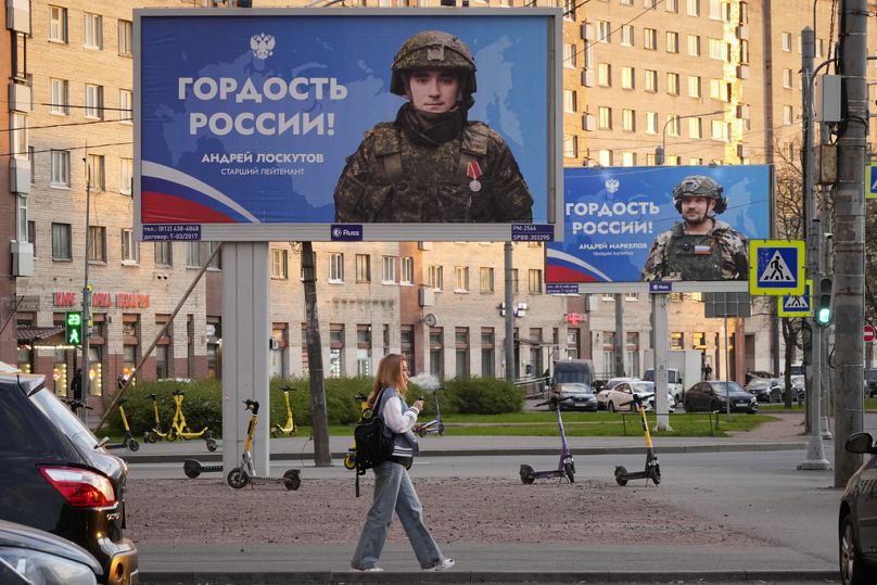 Eine Frau geht an Werbeplakaten vorbei, die russische Soldaten zeigen, die am Krieg in der Ukraine teilnehmen, mit der Aufschrift "Stolz Russlands", in St. Petersburg, 2024.